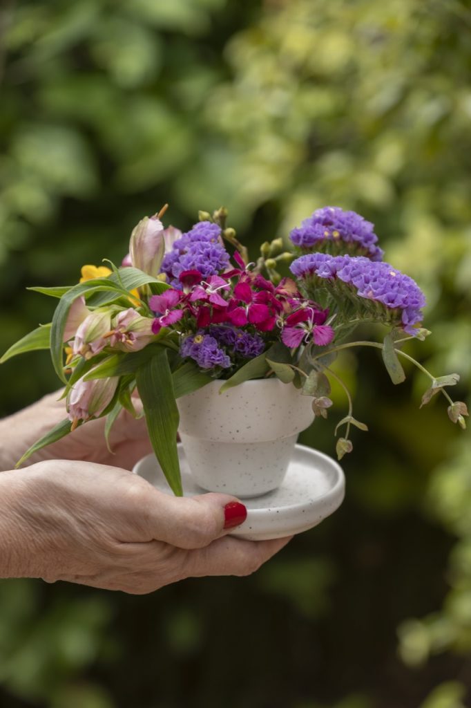 Xícara de café e pires, ambos de cerâmica branca, contendo arranjo de flores.