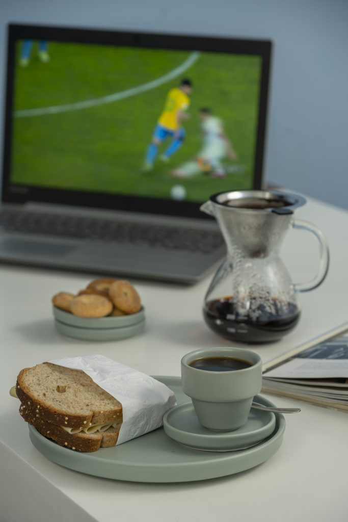 Em primeiro plano, vemos uma xícara de café dentro de um prato de sobremesa onde vemos um sanduíche no pão de forma. As peças são de cerâmica verde menta.