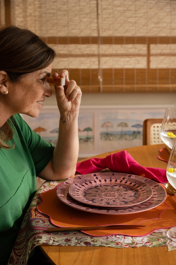 Imagem: mesa posta com pratos cor de rosa, jogo americano laranja, mini peras decorativas e taças onduladas.