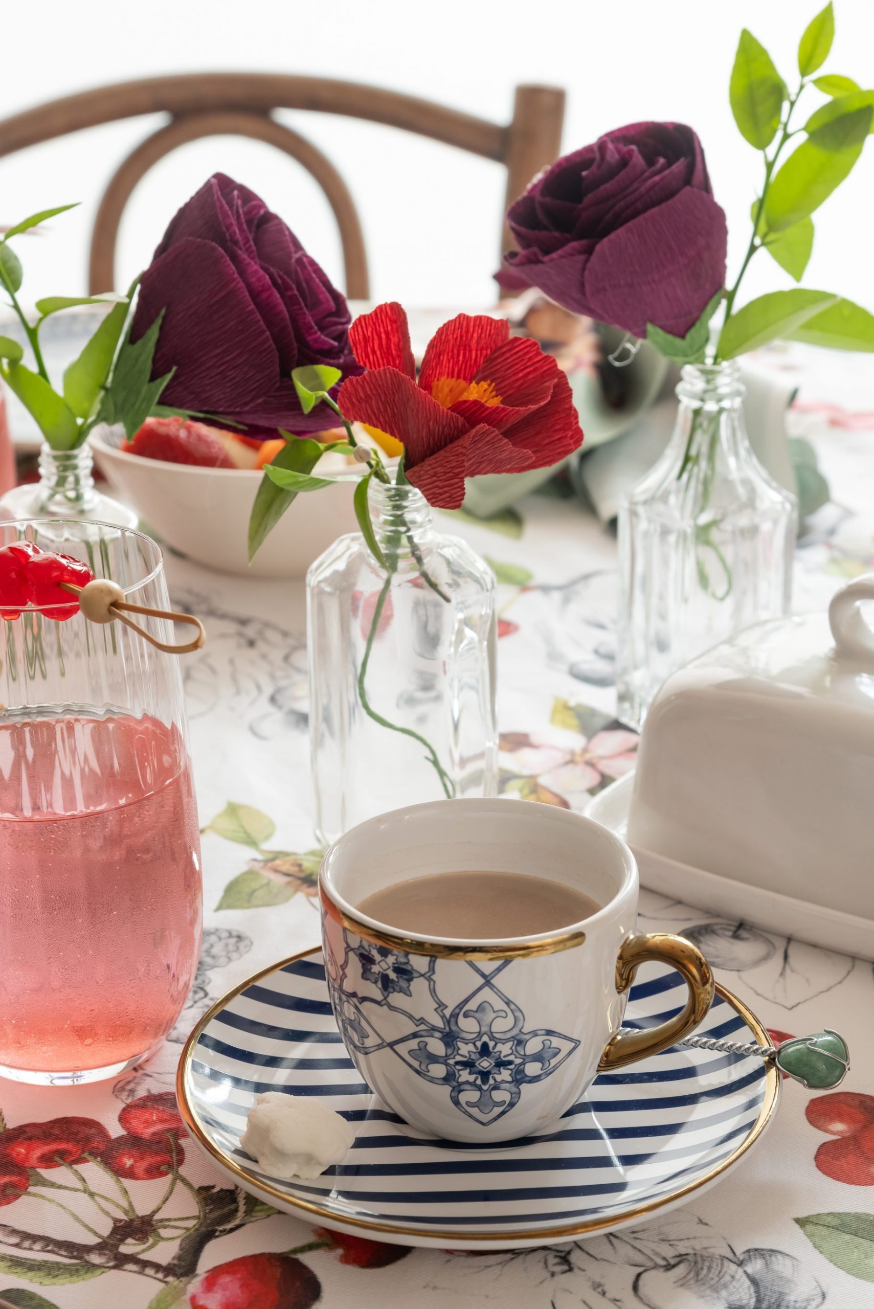Imagem: mesa de café da manhã com louças azuis, bowl de frutas e toalha de mesa de cerejas.