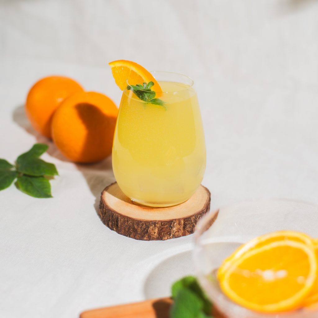 Imagem: copo de cristal da linha Easy da Oxford servido com drink sem álcool de cor amarela. Laranjas e rodelas de laranjas compõem a cena.