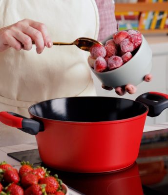 Imagem: caçarola verde sobre fogão de indução e bowl de morangos sendo despejados na panela.