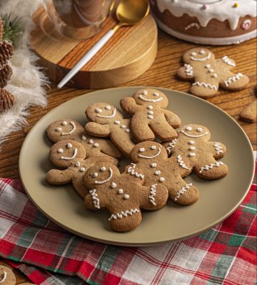 Imagem: biscoitos de Natal em formato de boneco em cima de prato verde em toalha de mesa xadrez vermelha.